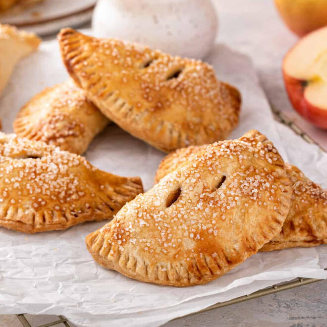 Golden apple hand pies with a crunchy outer crust dusted with coarse sugar, with a cinnamon-coloured filling peeking through the steam cuts in the top