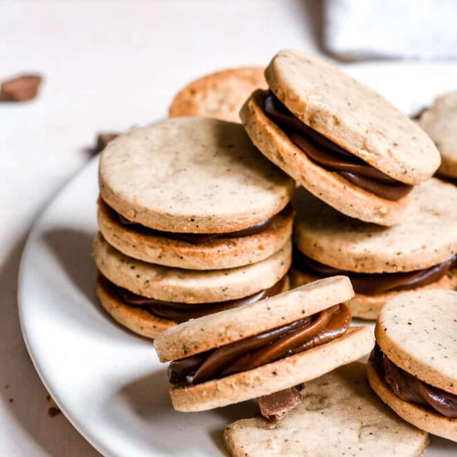 a plate of crunchy coin-like cookies, all sandwiched with a coffee-coloured ribbon of cream in the centre