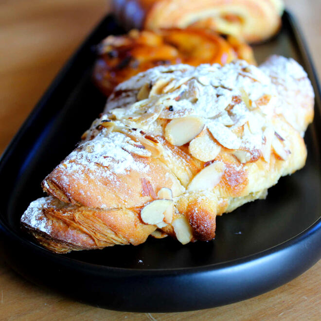 a flaky croissant with almond cream sandwiched between two halves, dusted with powdered sugar and almond slices